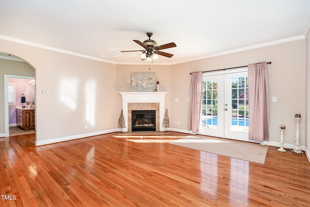 unfurnished living room featuring french doors, light hardwood / wood-style floors, ceiling fan, crown molding, and a fireplace