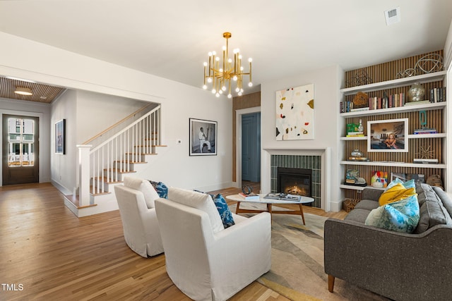 living room with a chandelier, a tiled fireplace, and light wood-type flooring