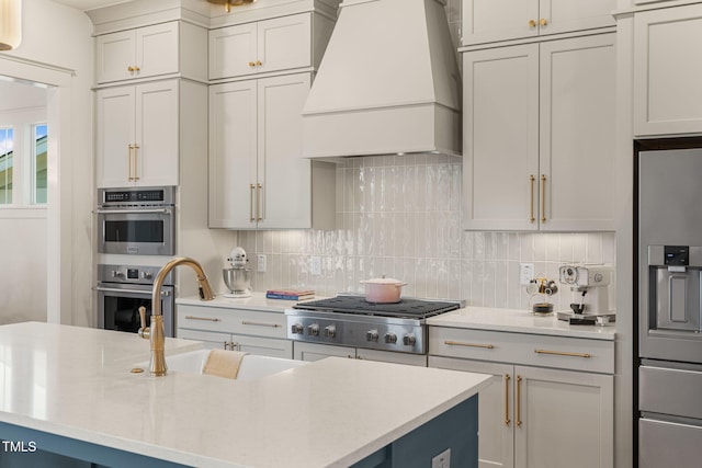 kitchen with custom range hood, backsplash, and an island with sink