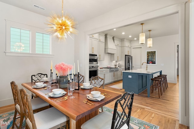 dining space with sink, light hardwood / wood-style floors, and an inviting chandelier