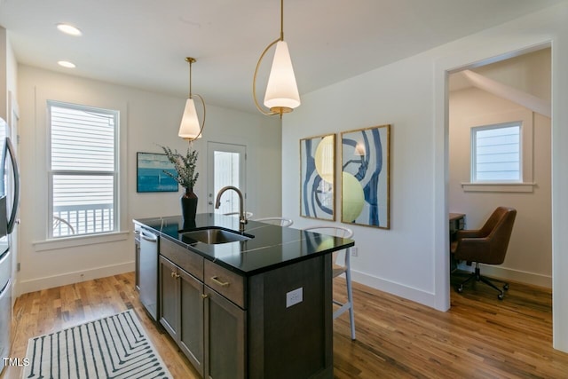 kitchen with appliances with stainless steel finishes, sink, hanging light fixtures, hardwood / wood-style flooring, and a kitchen island with sink