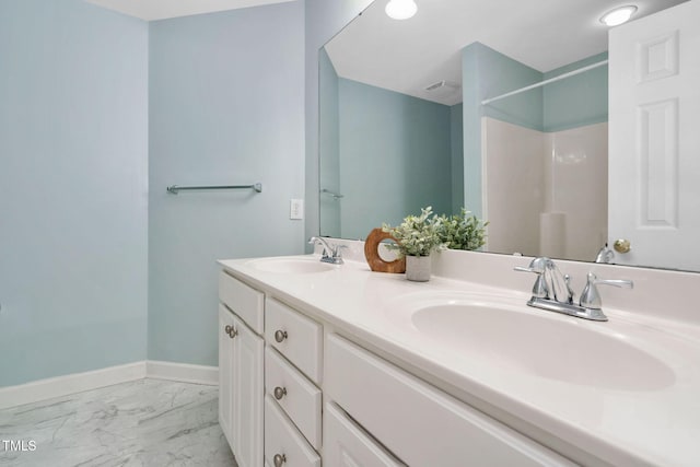 bathroom with marble finish floors, a shower, double vanity, and baseboards