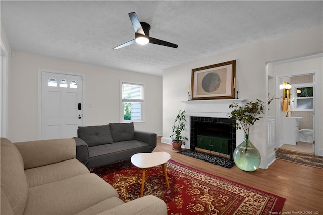 living room featuring a textured ceiling, wood-type flooring, a tile fireplace, and ceiling fan