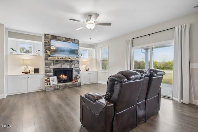 living room with dark hardwood / wood-style floors, ceiling fan, and a stone fireplace