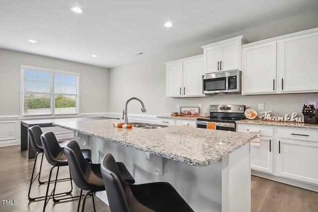 kitchen with a center island with sink, white cabinets, sink, hardwood / wood-style flooring, and stainless steel appliances