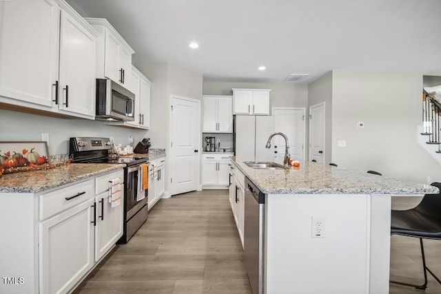 kitchen with appliances with stainless steel finishes, light stone counters, a kitchen island with sink, sink, and white cabinetry