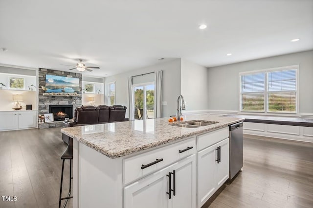 kitchen featuring dishwasher, sink, a stone fireplace, an island with sink, and white cabinets