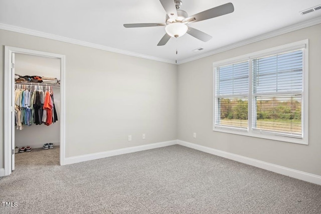 unfurnished bedroom with carpet flooring, ceiling fan, a walk in closet, a closet, and ornamental molding