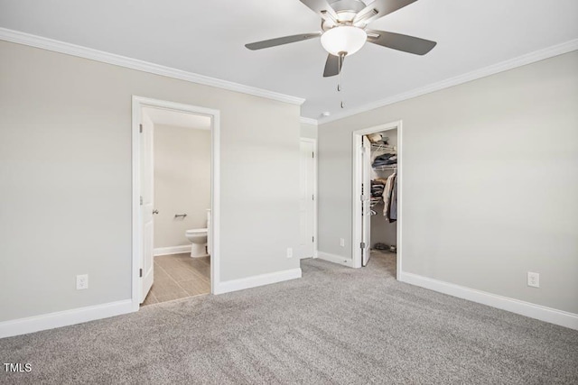 unfurnished bedroom featuring a walk in closet, ceiling fan, ornamental molding, connected bathroom, and light colored carpet