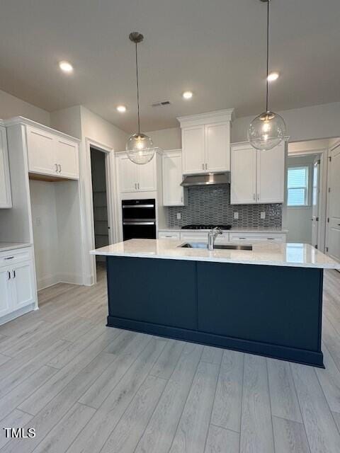 kitchen featuring hanging light fixtures, light hardwood / wood-style floors, an island with sink, white cabinets, and decorative backsplash