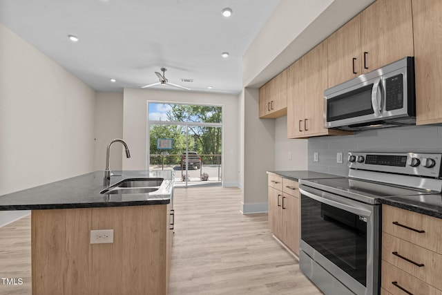 kitchen featuring an island with sink, stainless steel appliances, sink, light hardwood / wood-style floors, and tasteful backsplash