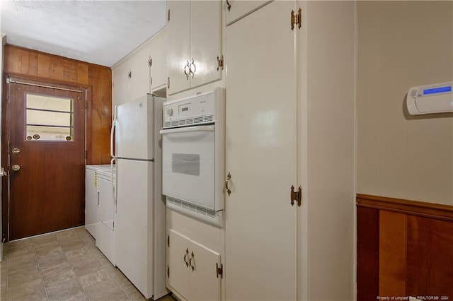 kitchen with white appliances, washer and dryer, white cabinetry, and wooden walls