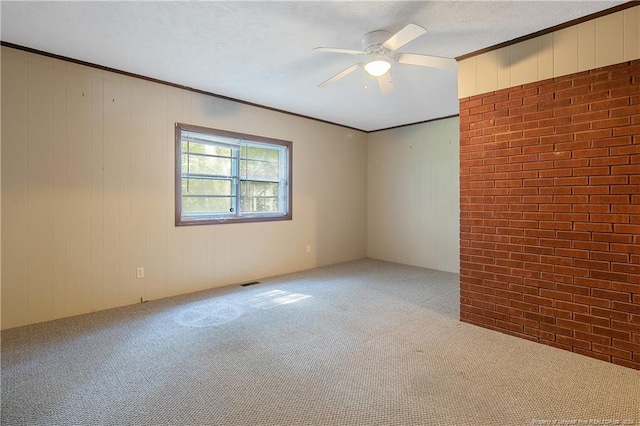 carpeted spare room with ceiling fan, crown molding, and wood walls