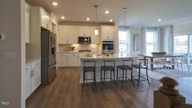 kitchen with a center island with sink, appliances with stainless steel finishes, hanging light fixtures, and dark hardwood / wood-style floors