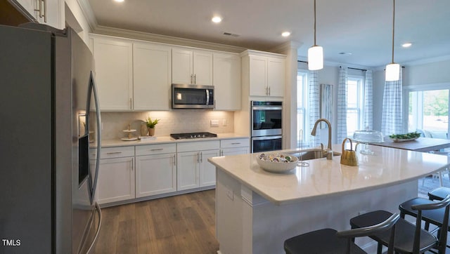 kitchen with a center island with sink, ornamental molding, sink, pendant lighting, and appliances with stainless steel finishes