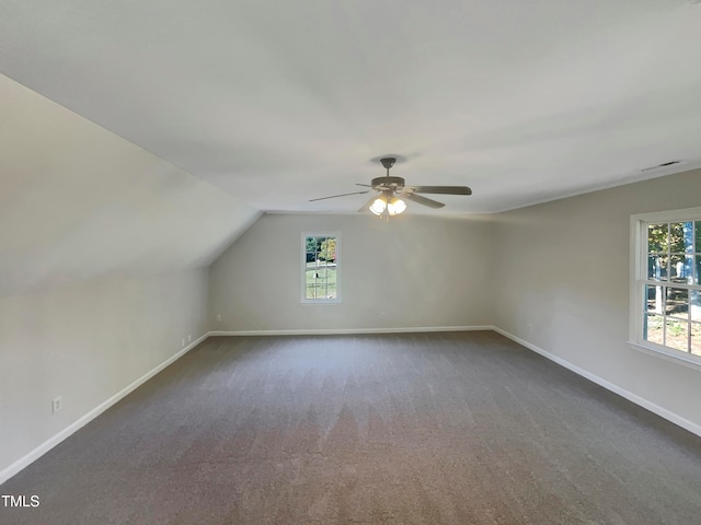 additional living space featuring vaulted ceiling, a wealth of natural light, dark carpet, and ceiling fan