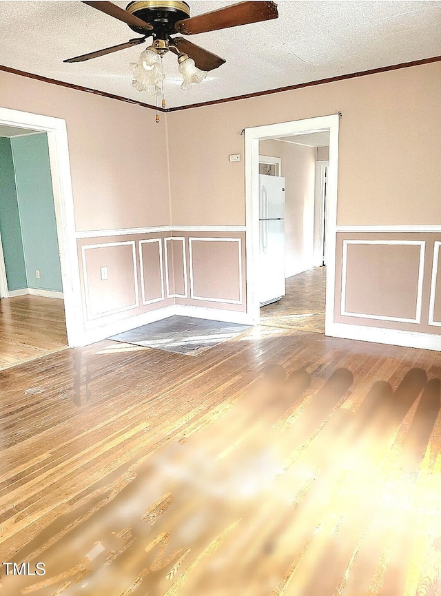 empty room with a textured ceiling, hardwood / wood-style flooring, ceiling fan, and crown molding