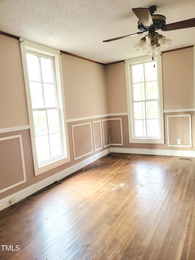 empty room featuring wood-type flooring, a healthy amount of sunlight, and ceiling fan