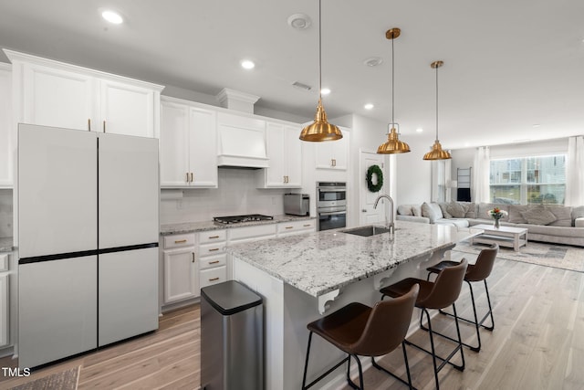 kitchen with appliances with stainless steel finishes, sink, light hardwood / wood-style floors, white cabinets, and a center island with sink