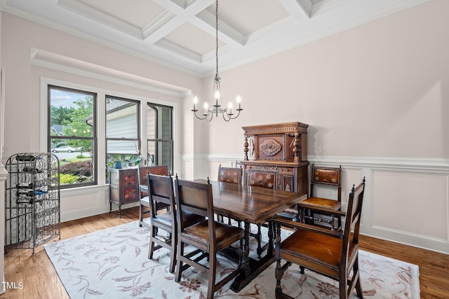 dining area featuring light hardwood / wood-style flooring, ornamental molding, a notable chandelier, and coffered ceiling