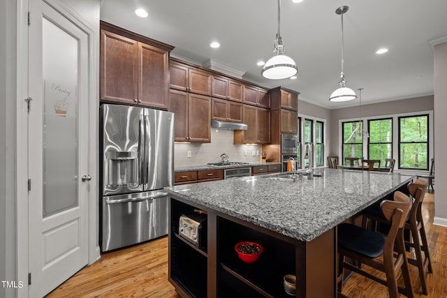 kitchen with light stone countertops, appliances with stainless steel finishes, light hardwood / wood-style flooring, and an island with sink