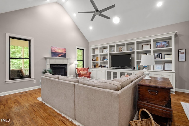 living room featuring a high end fireplace, light hardwood / wood-style flooring, a healthy amount of sunlight, and ceiling fan