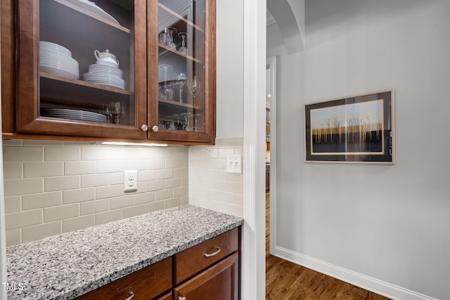 bar featuring light stone countertops, dark wood-type flooring, and backsplash