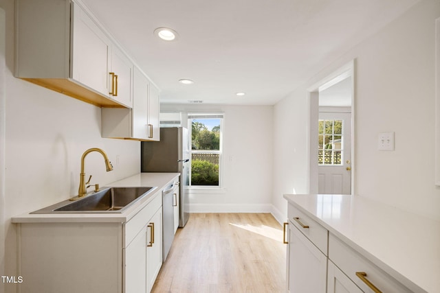 kitchen with stainless steel appliances, sink, light wood-type flooring, and white cabinets