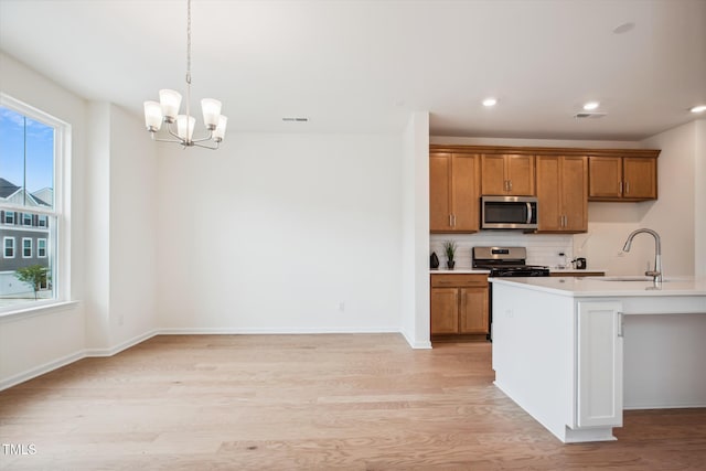 kitchen with sink, appliances with stainless steel finishes, a notable chandelier, light hardwood / wood-style floors, and an island with sink