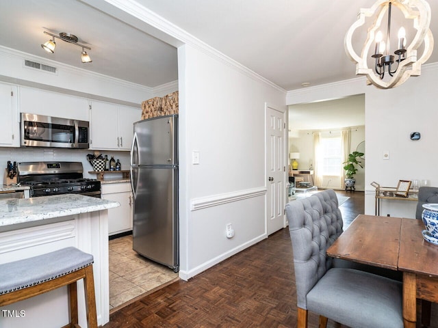 kitchen with dark parquet floors, appliances with stainless steel finishes, white cabinetry, light stone countertops, and decorative light fixtures