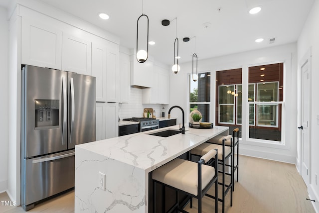 kitchen with pendant lighting, appliances with stainless steel finishes, sink, white cabinets, and a center island with sink