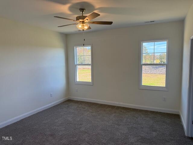 unfurnished room featuring dark colored carpet, a wealth of natural light, and ceiling fan