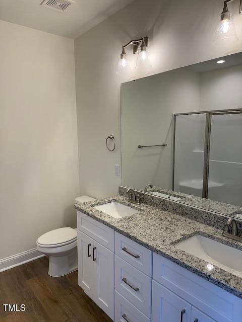 bathroom featuring hardwood / wood-style flooring, a shower with door, vanity, and toilet