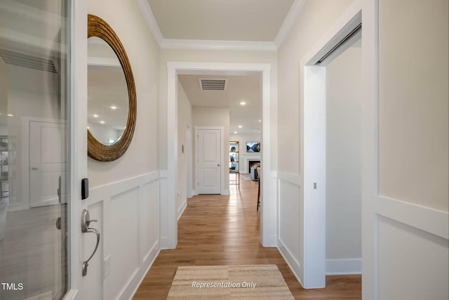 hallway featuring crown molding, visible vents, wood finished floors, and a decorative wall