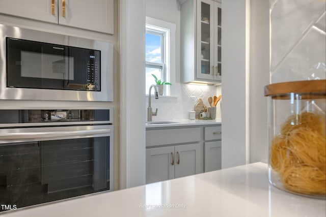 kitchen with decorative backsplash, glass insert cabinets, stainless steel oven, built in microwave, and a sink