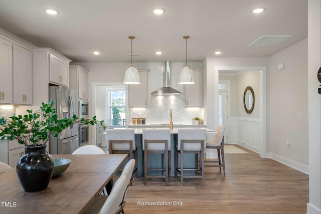kitchen with wall chimney range hood, decorative backsplash, light countertops, stainless steel appliances, and light wood-style flooring