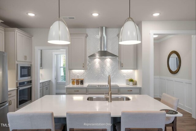 kitchen featuring a kitchen breakfast bar, tasteful backsplash, light countertops, stainless steel appliances, and wall chimney exhaust hood