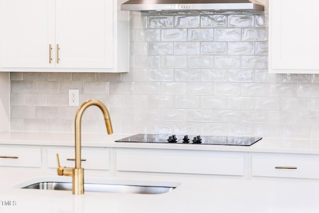 kitchen view of a sink, tasteful backsplash, ventilation hood, and white cabinets
