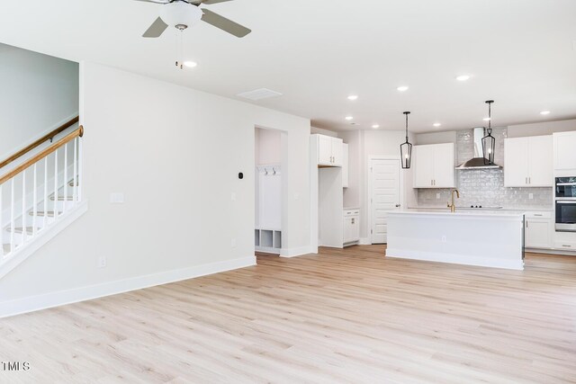 unfurnished living room with light wood-style floors, recessed lighting, a ceiling fan, stairs, and baseboards