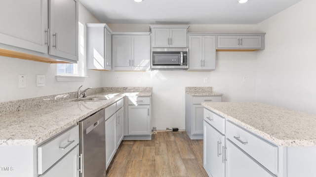 kitchen featuring sink, light stone countertops, light wood-type flooring, gray cabinets, and appliances with stainless steel finishes