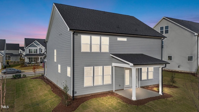 back house at dusk with a patio area and a yard