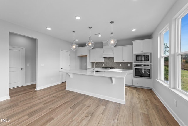 kitchen featuring sink, light hardwood / wood-style floors, decorative light fixtures, a kitchen island with sink, and black appliances