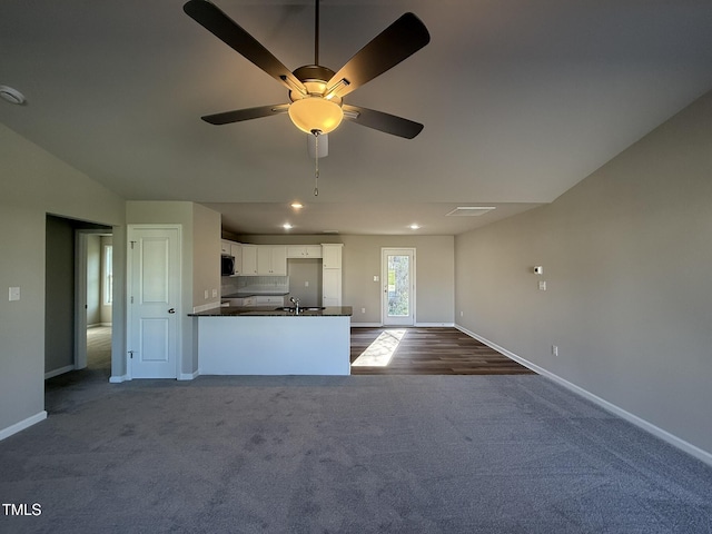 kitchen featuring white cabinetry, dark colored carpet, stainless steel microwave, dark countertops, and a peninsula