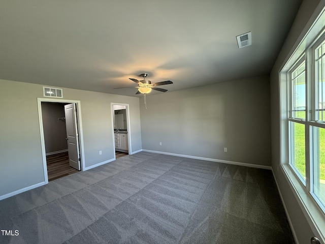 unfurnished bedroom with baseboards, visible vents, a walk in closet, and dark colored carpet