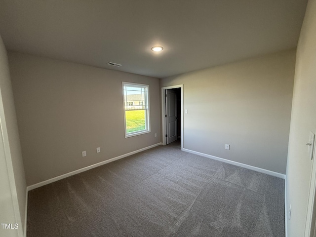 empty room with baseboards, visible vents, and dark colored carpet
