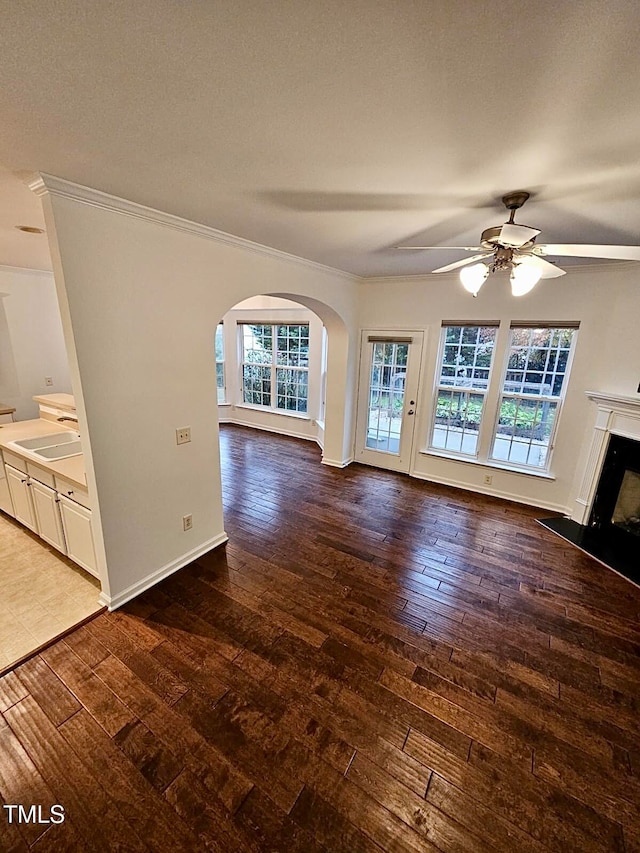 unfurnished living room featuring ceiling fan, crown molding, wood-type flooring, and sink