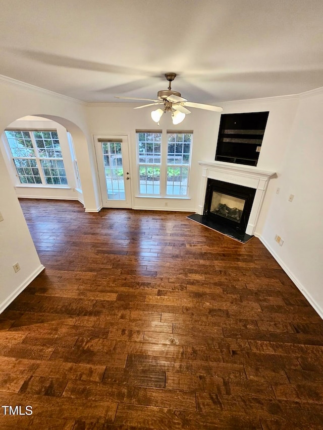 unfurnished living room featuring a wealth of natural light, crown molding, ceiling fan, and dark wood-type flooring