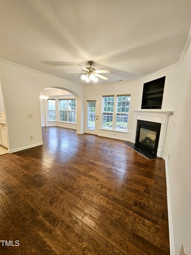 unfurnished living room featuring ceiling fan with notable chandelier, dark hardwood / wood-style flooring, plenty of natural light, and crown molding