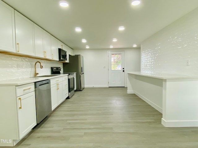 kitchen featuring appliances with stainless steel finishes, tasteful backsplash, sink, light hardwood / wood-style flooring, and white cabinets