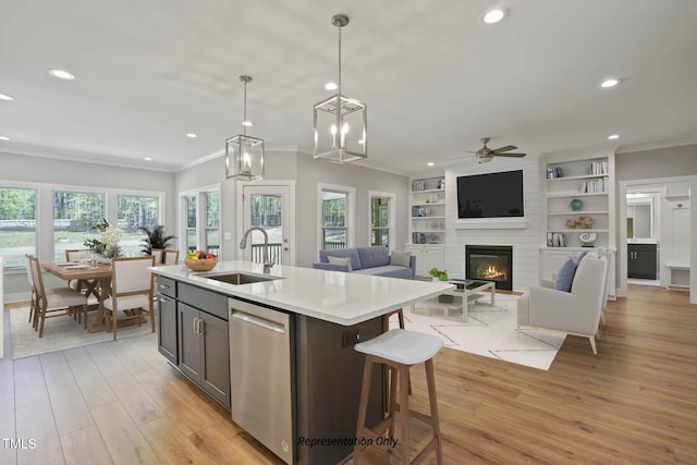 kitchen with dishwasher, an island with sink, sink, pendant lighting, and light wood-type flooring